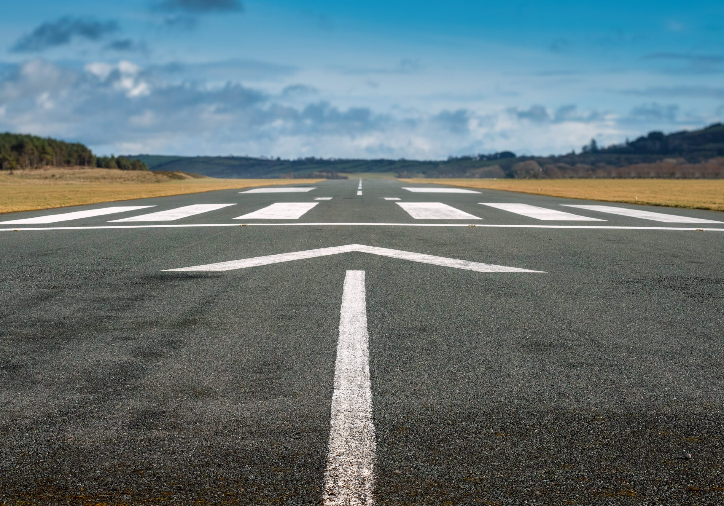 Small airport asphalt runway with markings for landings. Blue cloudy sky and fields around. Nobody.
